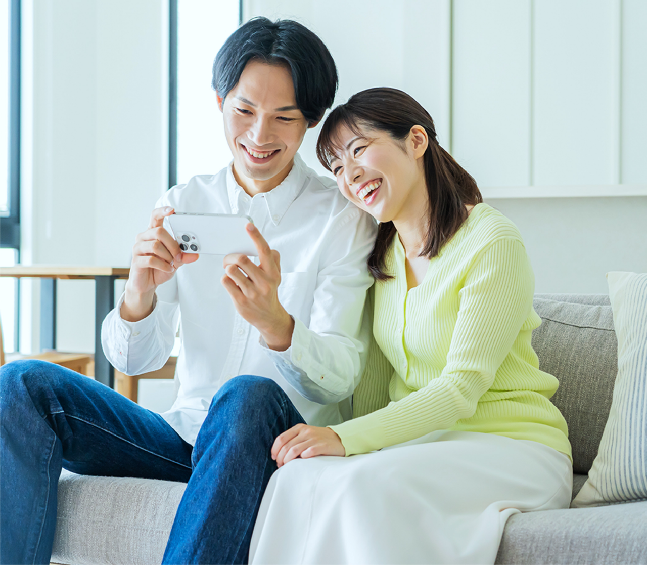 ソファに座る男女がスマートフォンを見ながら笑顔で楽しんでいる様子